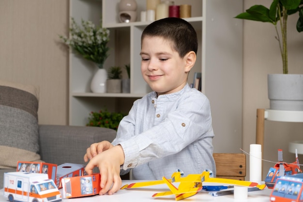 Een zesjarige jongen kleeft een papieren speelgoed aan Creativiteit en kinderen