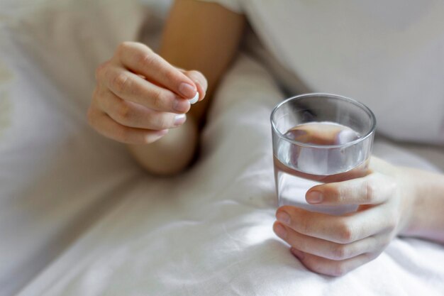 Een zieke jonge man houdt een pil en een glas water vast. medicijnen nemen.