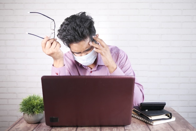 Een zieke jongeman met beschermend masker in gezicht die op laptop werkt