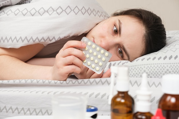 Een zieke vrouw ligt in bed en houdt pillen in haar hand