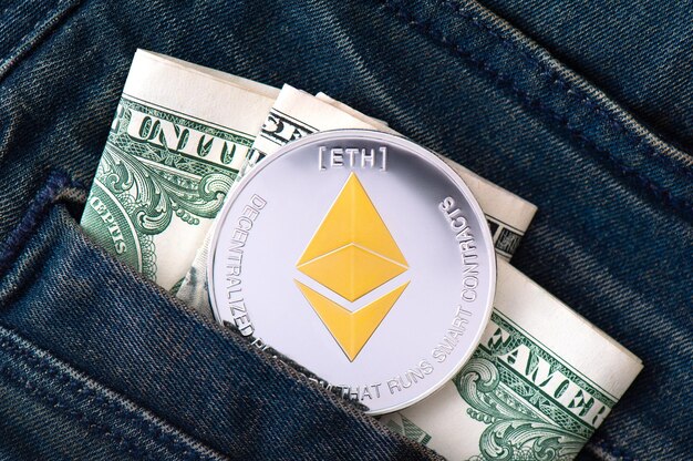 Een zilveren fysieke Ethereum-munt met gouden symbool en gevouwen Amerikaanse dollars steekt uit de zak van spijkerbroek close-up Geld besparen in cryptocurrency concept Zakelijke achtergrond