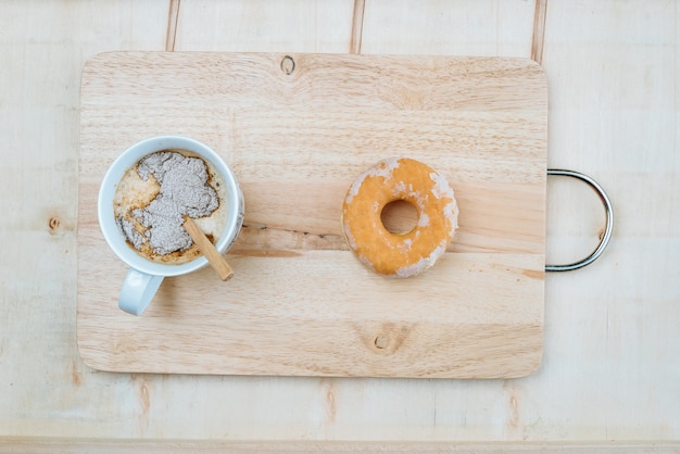 Een zoete kop koffie geplaatst op een houten bord samen met een donut.