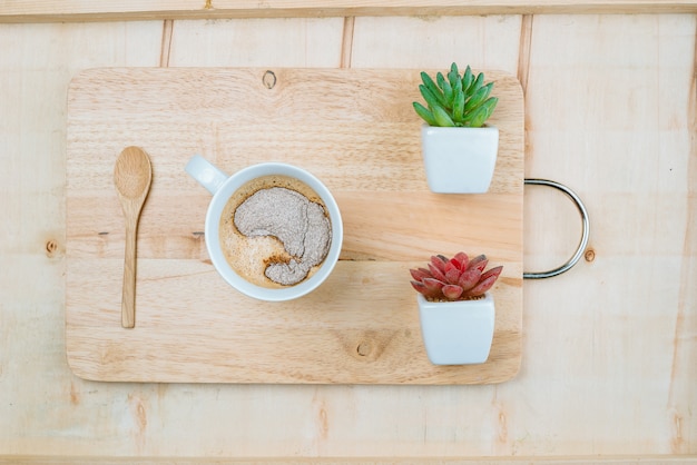 Een zoete kop koffie geplaatst op een houten bord versierd met twee planten