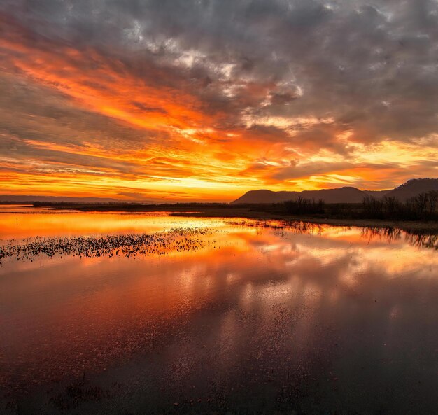 een zonsondergang met een weerspiegeling van een berg en wolken in het water