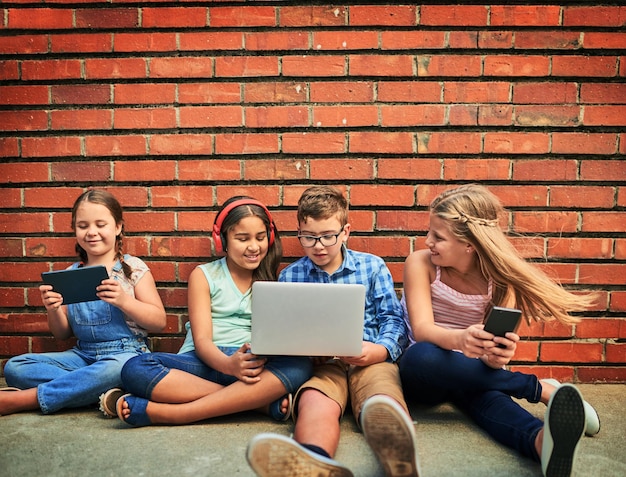 Een zorgeloze en verbonden jeugd delen Shot van een groep jonge kinderen die digitale apparaten gebruiken tegen een bakstenen muur