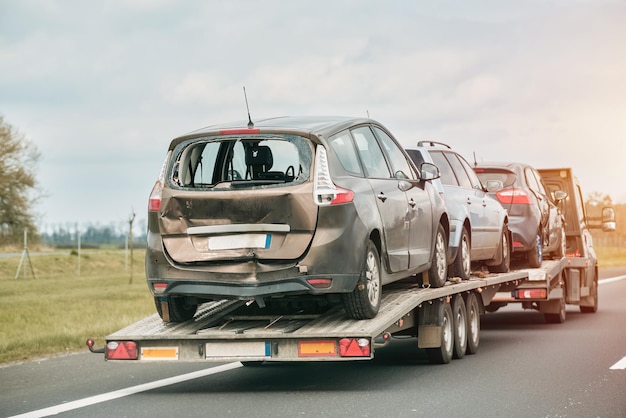 Een zwaar beschadigde auto op een aanhangwagen wordt getrokken door een sleepwagen