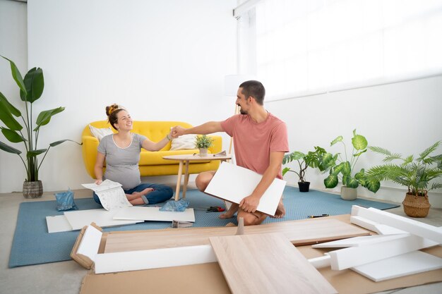 Een zwanger echtpaar houdt elkaar gelukkig bij de hand terwijl ze meubels in het nieuwe huis monteren