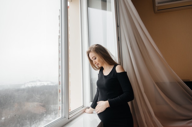 Een zwanger meisje ademt frisse lucht uit het raam.
