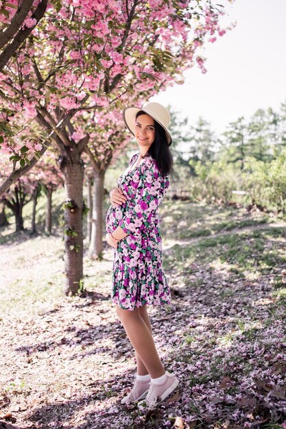 Een zwanger meisje in een jurk bij de sakura in de tuin