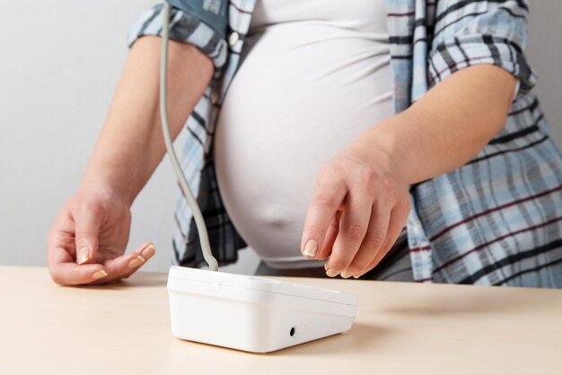 Een zwanger meisje meet haar bloeddruk met een tonometer Tijdens de zwangerschap is het belangrijk om de bloeddruk te controleren