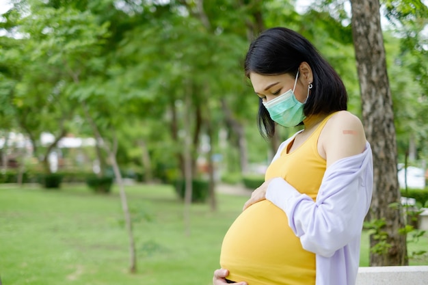 Een zwangere moeder in vrijetijdskleding staat naar haar buik te kijken en toont een pleister op haar schouder na vaccinatie.