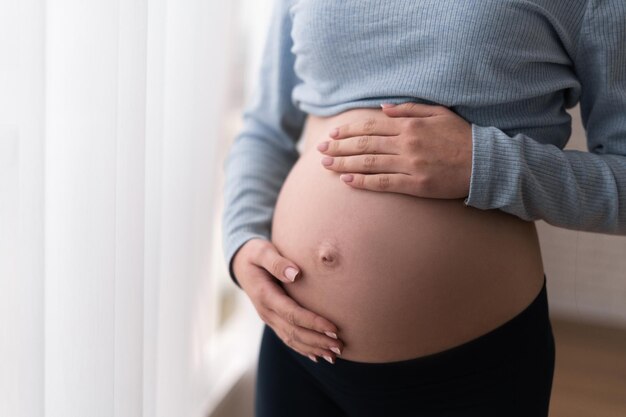 Een zwangere staat bij het raam Buik close-up Handen raken hem aan Het concept van communicatie met de baby vóór de bevalling