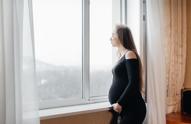 Een zwangere vrouw ademt frisse lucht uit het raam