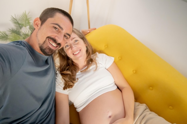 Foto een zwangere vrouw en haar man fotograferen zichzelf thuis met de mobiele telefoon