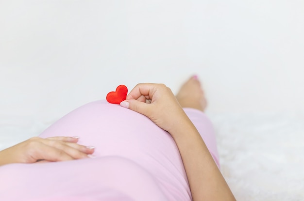Een zwangere vrouw houdt een hart vast.