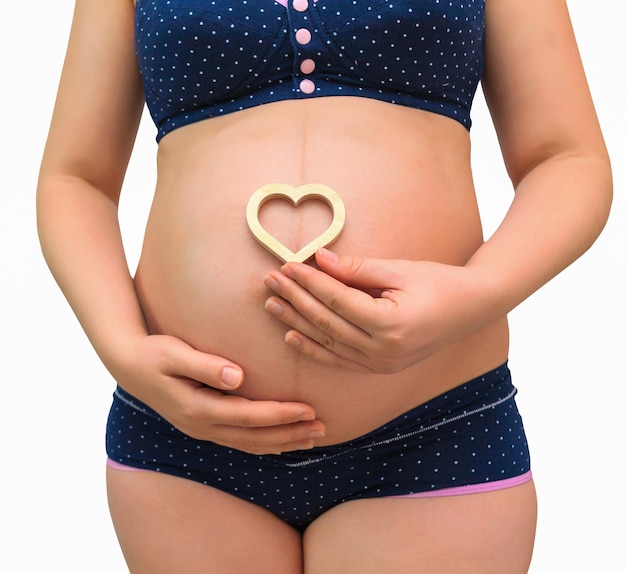 Een zwangere vrouw houdt een hartsymbool op de achtergrond van haar buik