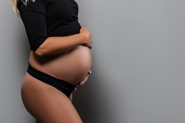 Een zwangere vrouw houdt haar handen op haar buik op een grijze achtergrond Zwangerschap moederschap voorbereiding en verwachting concept