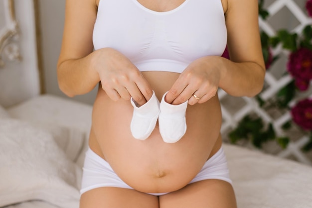 Een zwangere vrouw houdt witte slofjes in haar handen Een jonge vrouw in wit ondergoed