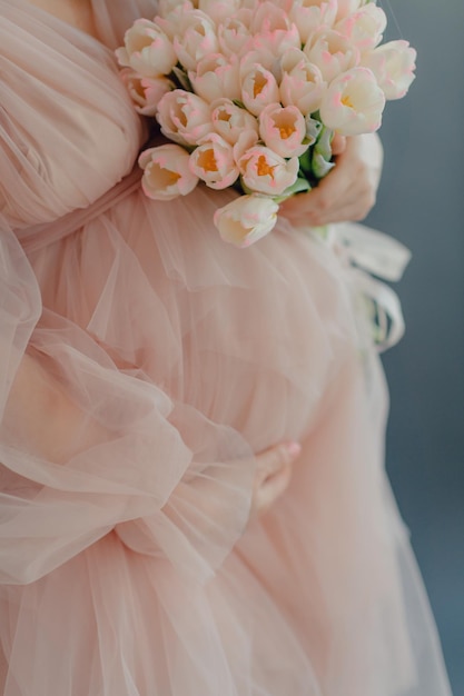Een zwangere vrouw in een roze jurk houdt een boeket bloemen vast