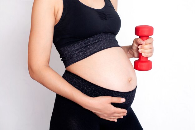 Een zwangere vrouw in een sportuniform houdt een halter in haar hand