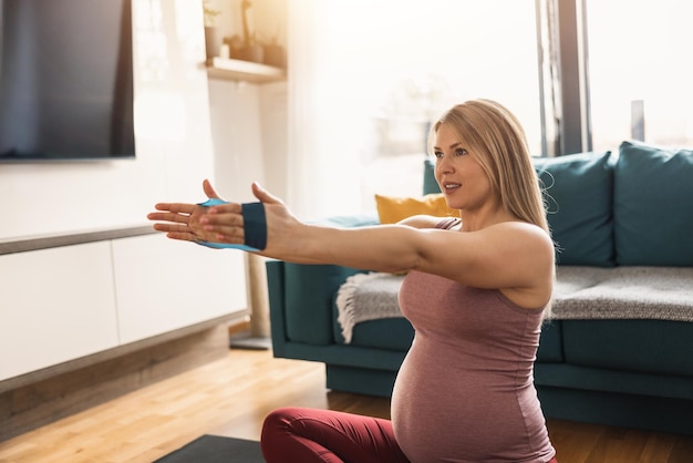 Foto een zwangere vrouw in sportkleding is aan het stretchen met een elastiekje en aan het sporten om het welzijn in haar woonkamer te bevorderen.