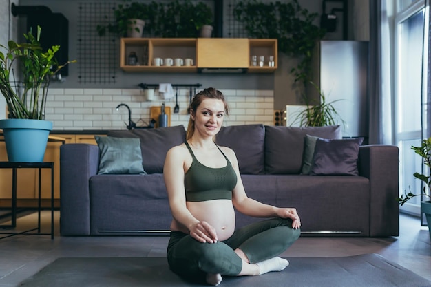 Een zwangere vrouw mediteert en beoefent thuis yoga in lotushouding