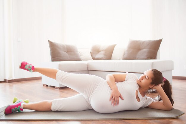 Een zwangere vrouw werkt thuis op een yogamat uit. Zwangerschap en sport.