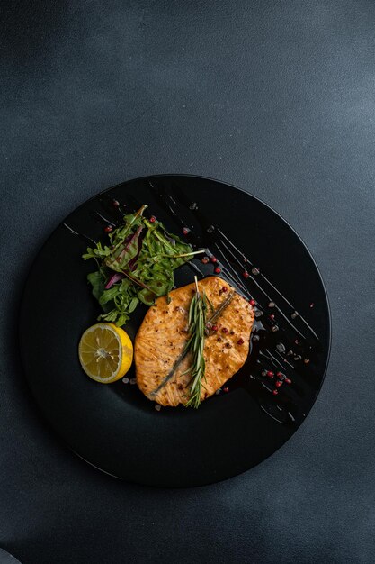 Een zwart bord met daarop een gegrilde zalm en een groen blad aan de zijkant.