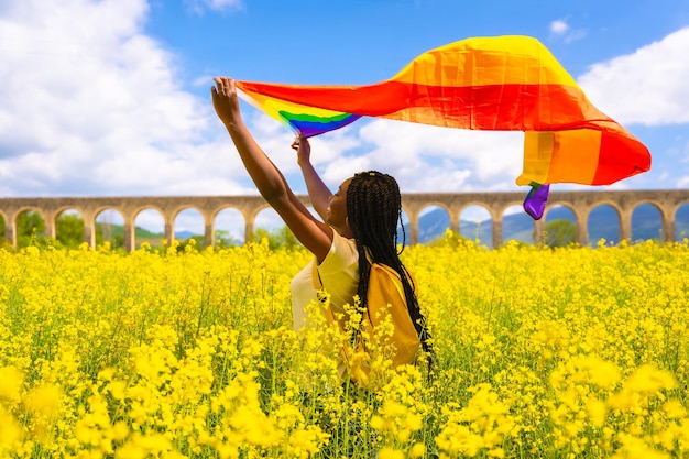 Een zwart etnisch meisje met vlechten met de LGBT-vlag in een bloemenveld