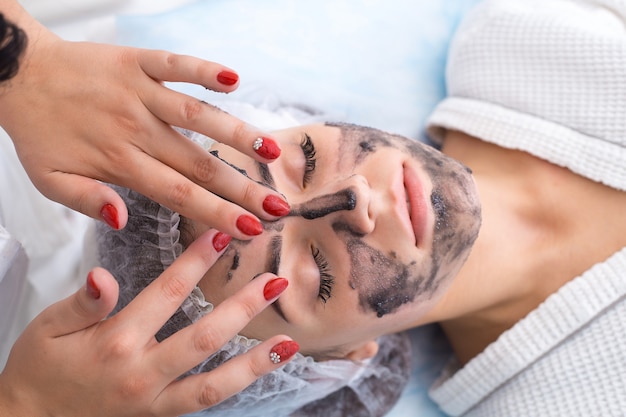 Foto een zwart masker op het gezicht van de patiënt tekenen. schoonheidssalon.