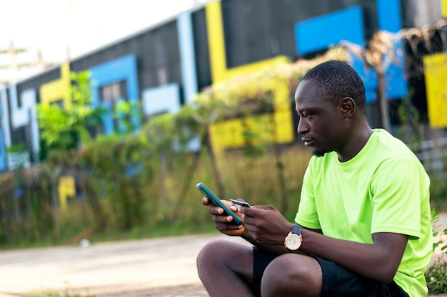 Een zwarte Afrikaanse man die op de grond zit en naar zijn mobiele telefoon kijkt