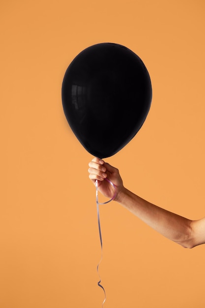 Een zwarte ballon in de hand van een meisje op een oranje achtergrond Halloween-concept