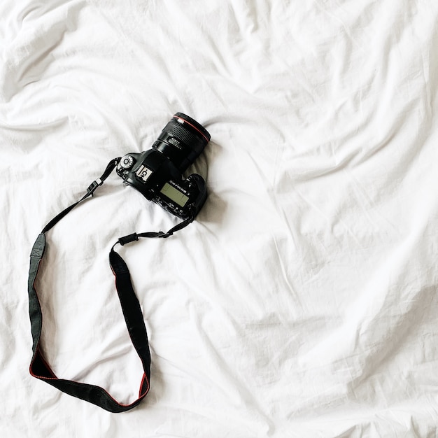 Een zwarte camera liggend op bed met wit linnen