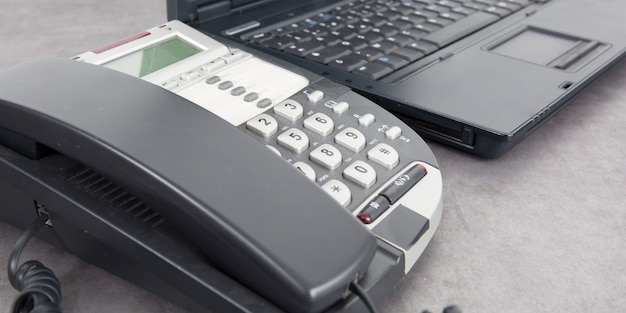 Een zwarte draadgebonden telefoon op het bureau naast laptop in bureau