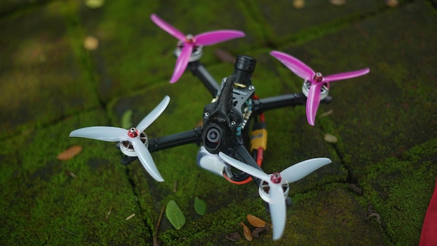 Foto een zwarte drone met roze vleugels en een zwarte afstandsbediening op de grond.