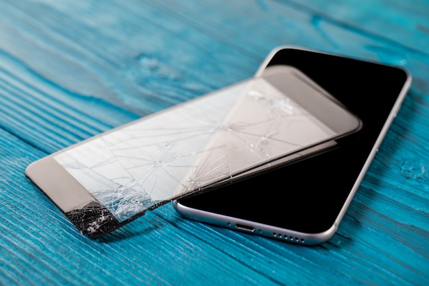 Een zwarte mobiele telefoon is gebroken scherm op hout achtergrond.