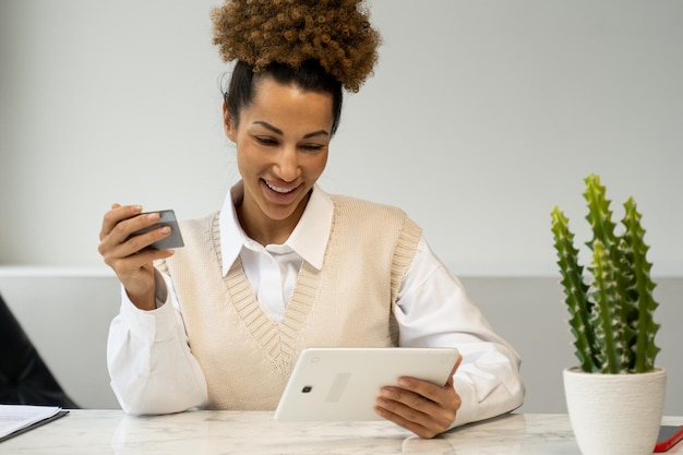 Een zwarte vrouw met een creditcard doet een online betaling met behulp van een tablet jonge vrouw met krullend haar