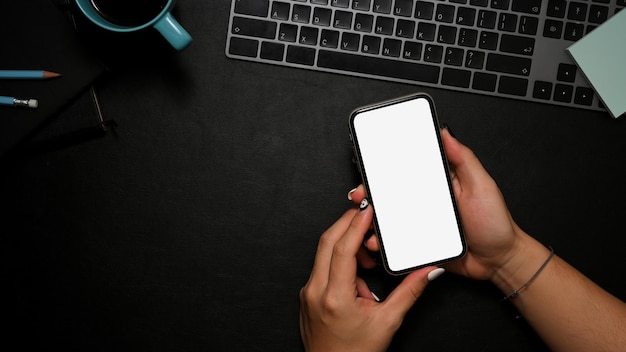 Een zwarte werktafel met kopieerruimte en vrouwelijke handen die een smartphonemodel boven haar bureau houden