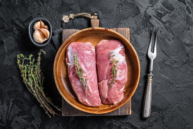 Eendenborstfilet in houten plaat, rauwe steaks van gevogelte. zwarte achtergrond. bovenaanzicht.