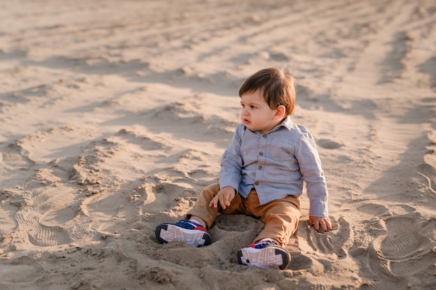 Eenjarige jongen zit in het zand, lacht en speelt.