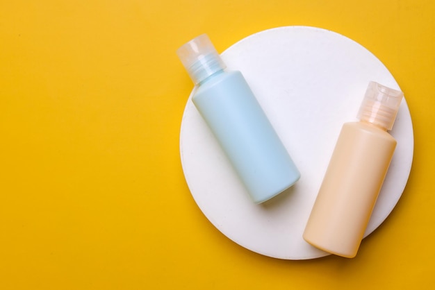 Eenvoud van twee cosmetische lege flessen op rond voetstuk geïsoleerd op gele achtergrond