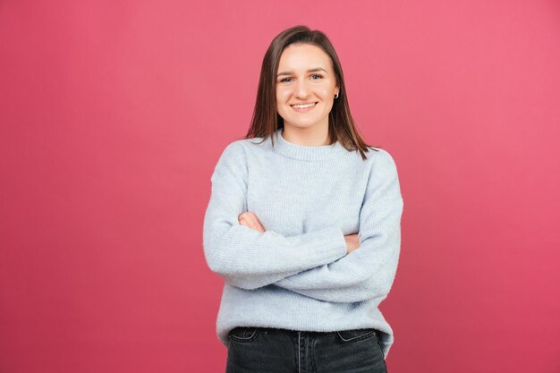 Eenvoudig portret van een mooi meisje dat met gekruiste armen staat terwijl ze naar de camera lacht