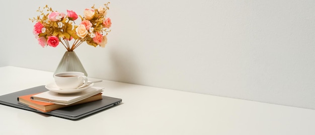 Eenvoudig wit bureau met koffiekopjes boeken laptop bloemenvaas en kopieerruimte over witte muur