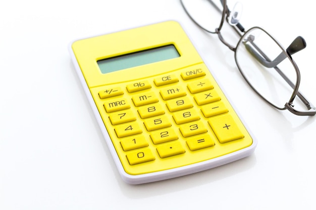 Eenvoudige gele rekenmachine met leesbril op een witte achtergrond.