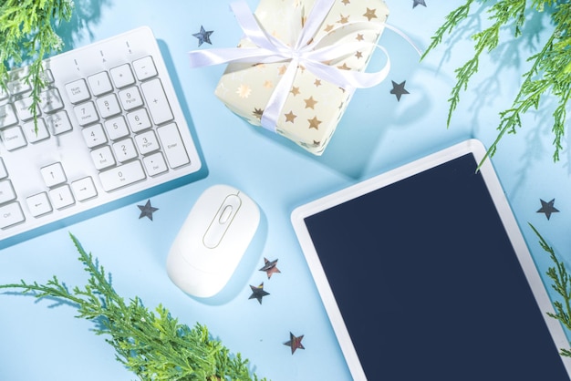 Eenvoudige minimale kerst kantoor achtergrond. Moderne hooggekleurde lichtblauwe achtergrond met office pc-toetsenbord, muis, tablet-pc, zilveren feestelijke sterren en kerstboomtakken, flatlay frame