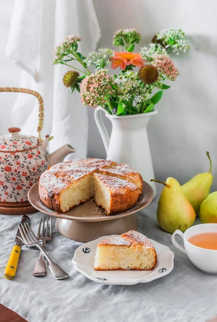Eenvoudige taart met peren en poedersuiker boeket bloemen theepot geserveerd gedekte tafel voor thee drinken
