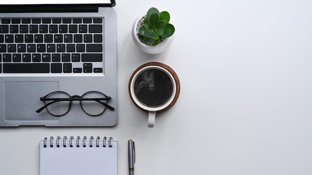 Eenvoudige werkplek met computer laptop koffiekopje glazen notebook en plant op wit bureau