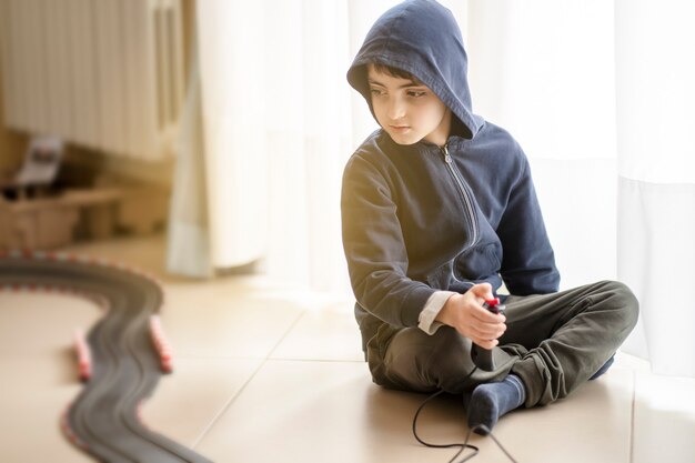 Eenzaam kind dat op de grond zit, speelt met een elektrische baan tijdens lockdown