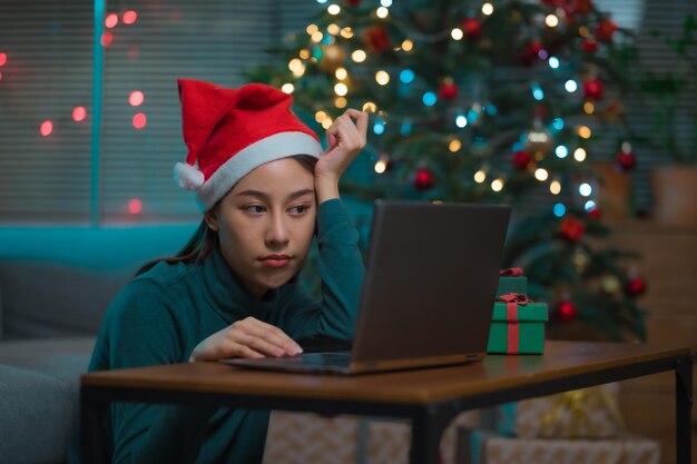 Eenzame Aziatische vrouw viert Kerstmis alleen thuis zittend op de vloer met behulp van laptop