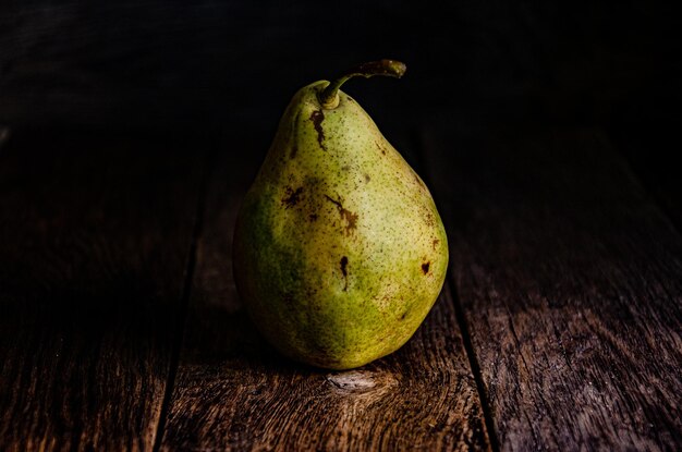 Eenzame groene peer op een houten keukentafel tegen een donkere achtergrond.